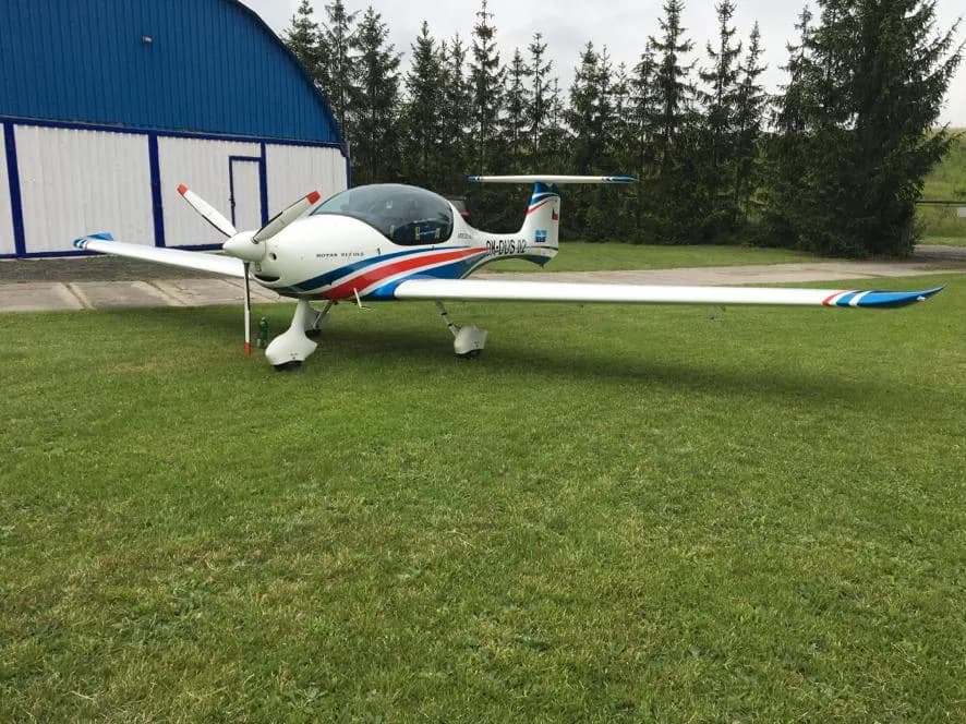 Letoun Atec 321 Faeta zaparkovaný na trávě u modrého hangáru