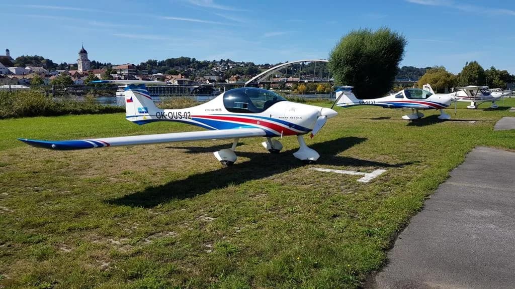 Letoun Atec 321 Faeta zaparkovaný na travnaté ploše u řeky