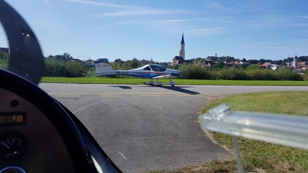 Pojíždění letadla po letišti s obcí v pozadí